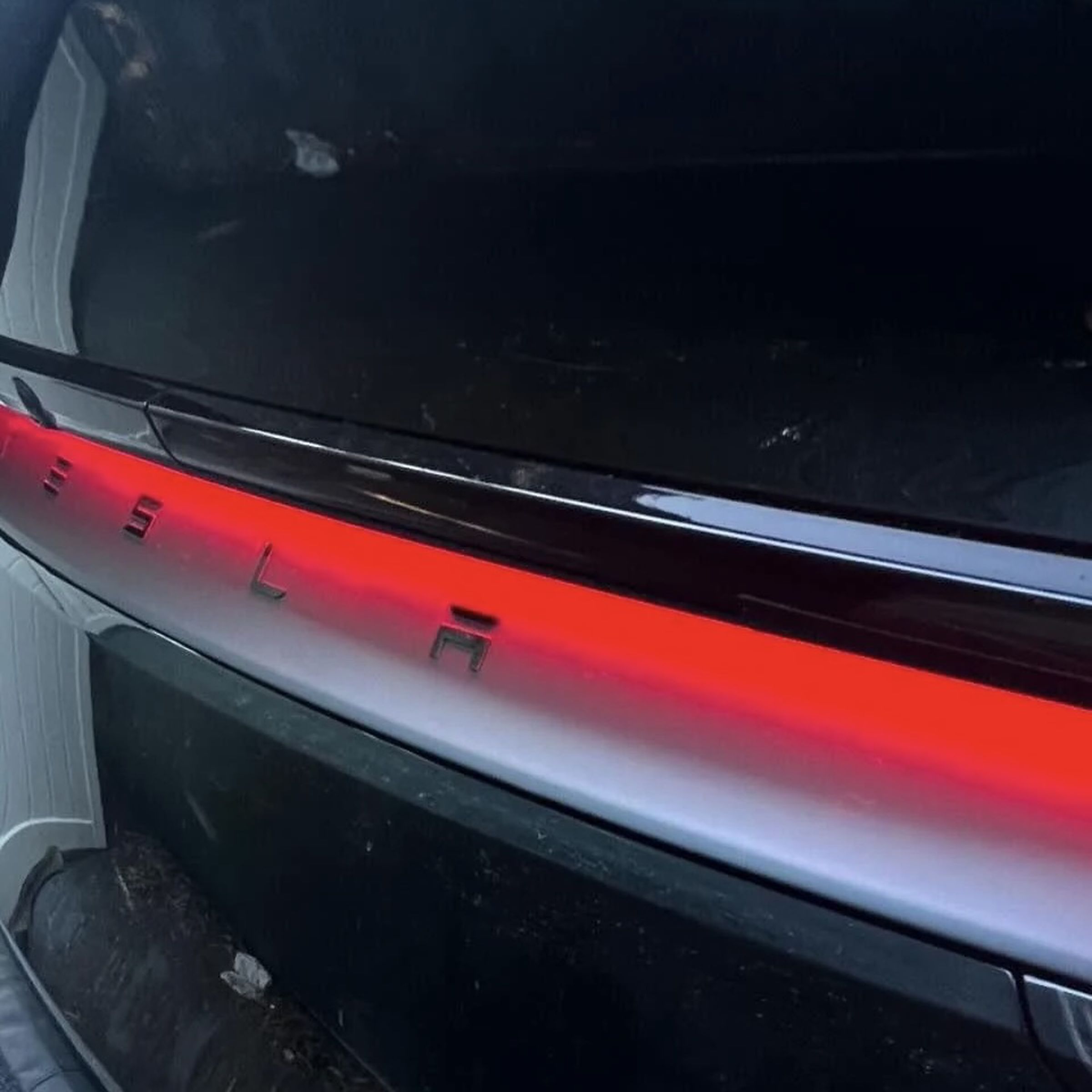 Close-up of a red-lit white light bar on the tail of a black SUV with TESLA printed in the center of the bar.