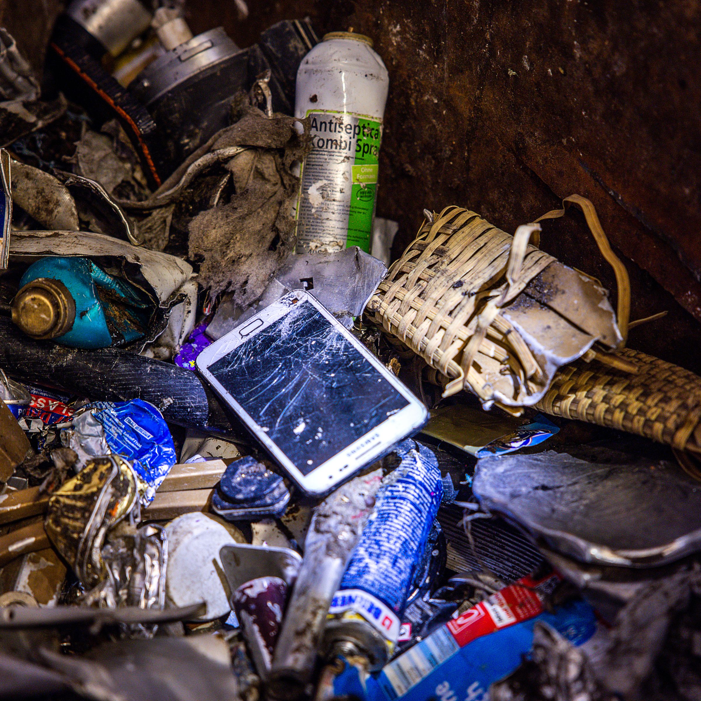 A cellphone with a cracked screen seen in a pile of trash.