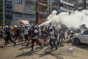 FILE - Anti-coup protesters run as one of them discharges a fire extinguisher to counter the impact of tear gas fired by riot policemen in Yangon, Myanmar, Wednesday, March 3, 2021. As Feb. 1, 2023, marks two years after Myanmar’s generals ousted Aung San Suu Kyi’s elected government, thousands of people have died in civil conflict and many more have been forced from their homes in a dire humanitarian crisis.