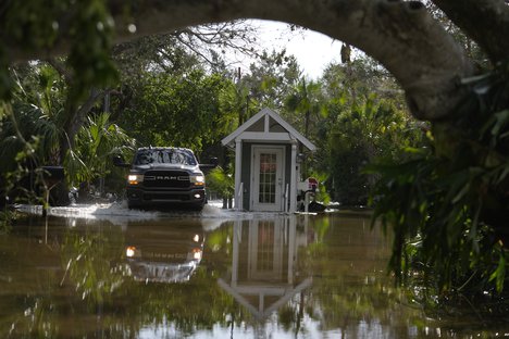 A pick up drives past a guard gate on a flooded street in Siesta Key, Fla., following the passage Hurricane Milton, Thursday, Oct. 10, 2024.