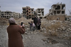 A Syrian man Mohammed Salam, 32, poses for a picture with his family in front of his destroyed house which destroyed during the civil war in the neighbourhood of Jobar, in Damascus, Syria, Saturday, Dec. 21, 2024.