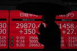 A man wearing a protective mask walks in the rain in front of an electronic stock board showing Japan's Nikkei 225, Tokyo