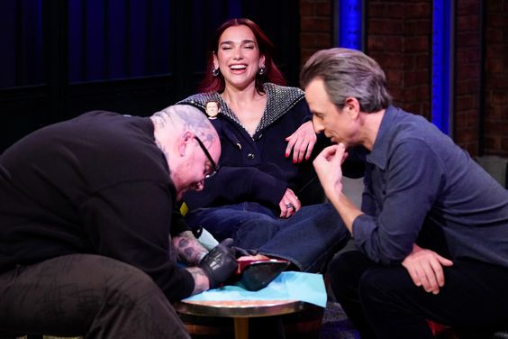 LATE NIGHT WITH SETH MEYERS -- Episode 1467 -- Pictured: (l-r) Tattoo artist Keith Scott "Bang Bang" McCurdy, musician Dua Lipa, host Seth Meyers during a segment on January 9, 2024 