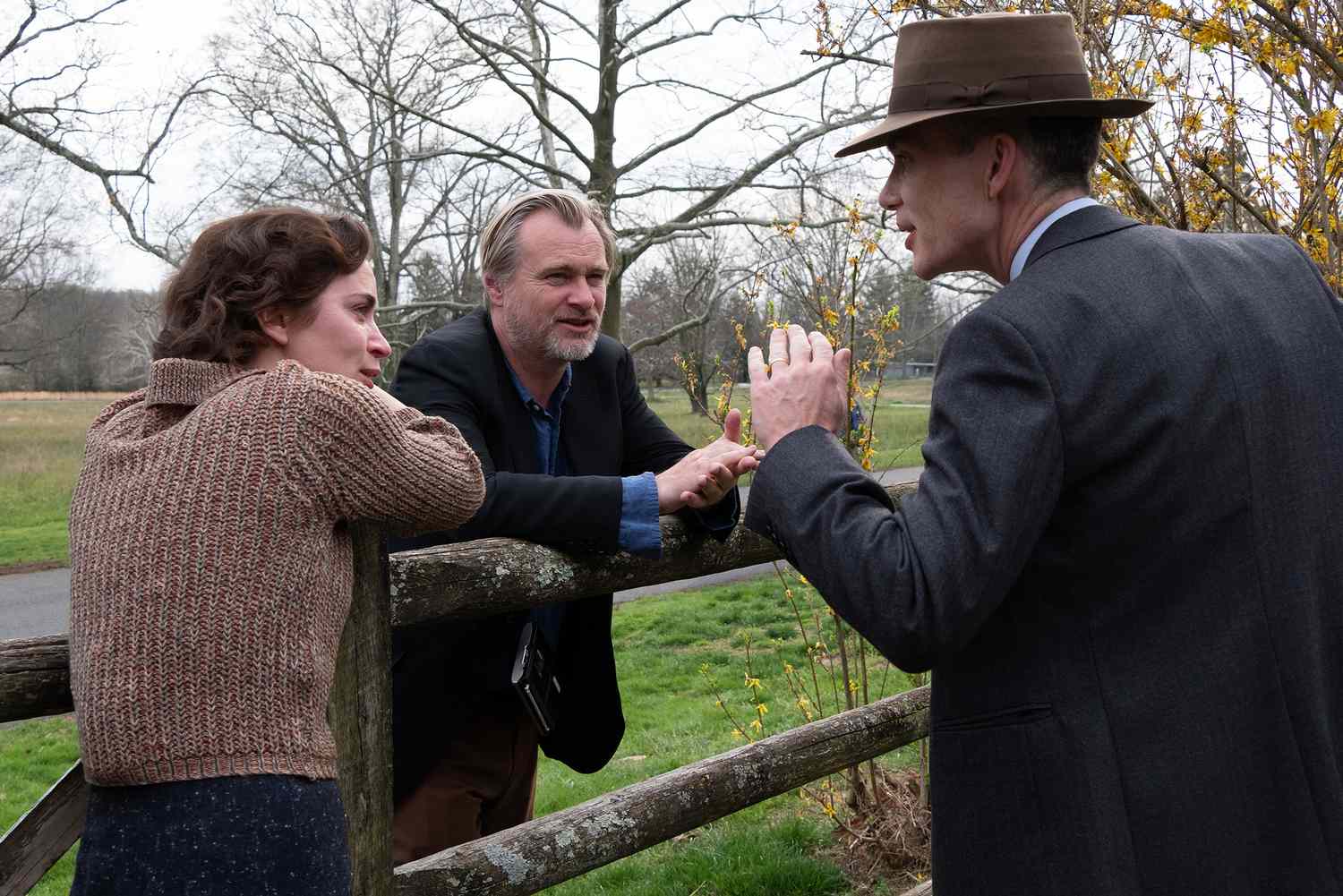 L to R: Emily Blunt (as Kitty Oppenheimer) with writer, director, and producer Christopher Nolan and Cillian Murphy (as J. Robert Oppenheimer) on the set of OPPENHEIMER.