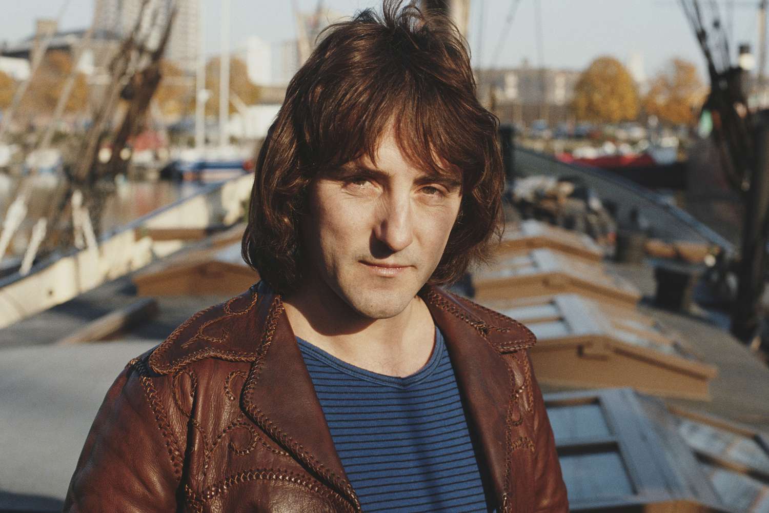 English singer-songwriter and former Wings and Moody Blues guitarist, Denny Laine posed wearing a leather jacket outside near an harbor 1981.