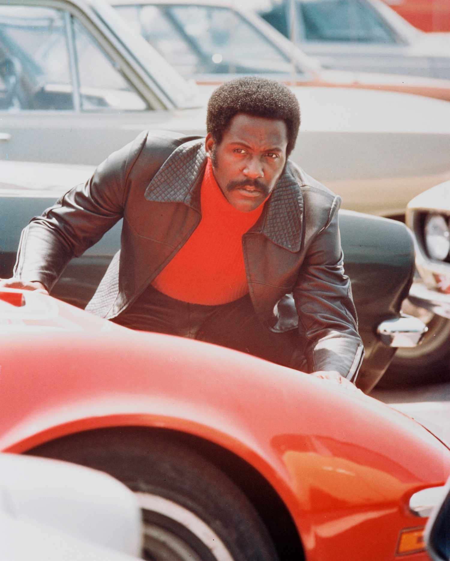 Richard Roundtree, US actor, crouching behind a red sports car in a publicity still issued for the film, 'Shaft', 1971. The blaxploitation film, directed by Gordon Parks (1912-2006), starred Roundtree as 'John Shaft'.