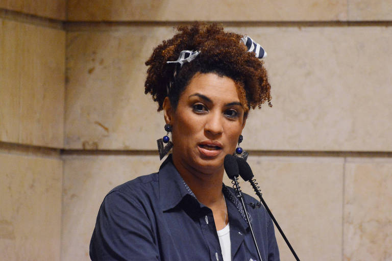 Na imagem, Marielle discursa no púlpito da Câmara Municipal. Ela é mulher negra, jovem e com o cabelo black power