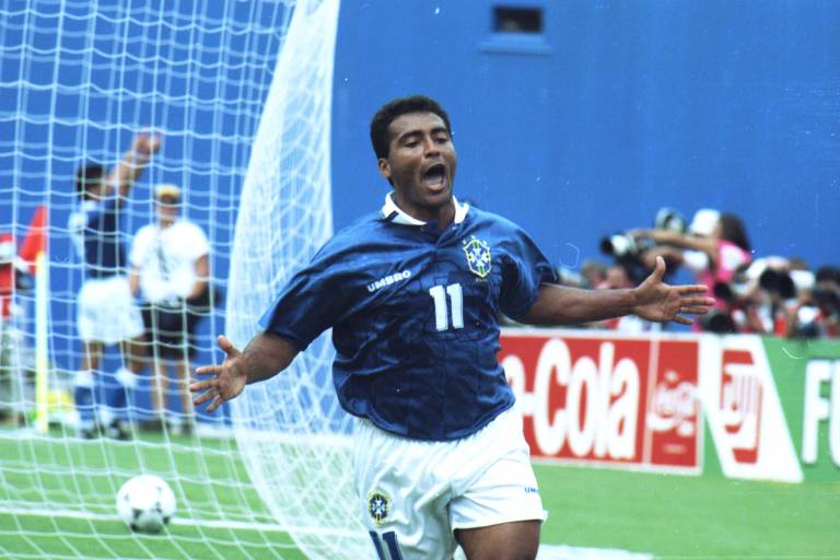 O jogador Romário, vestindo o uniforme azul e branco da seleção, corre de braços abertos, comemorando o gol