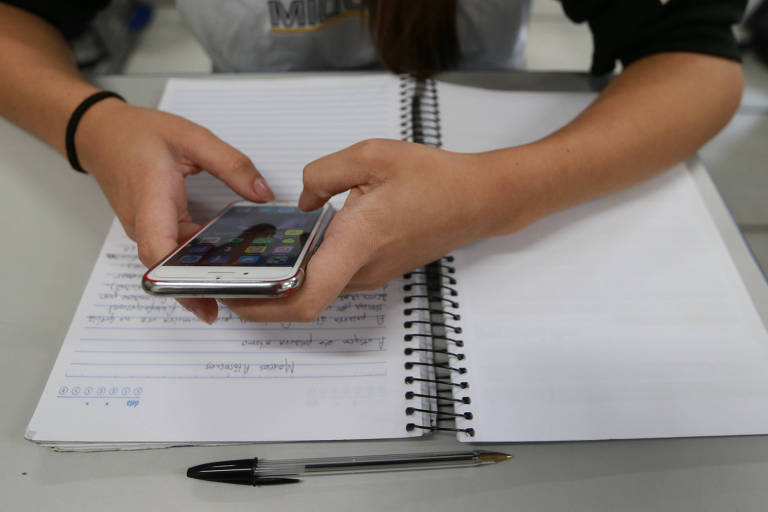 Estudante mexe com o celular em cima de caderno aberto