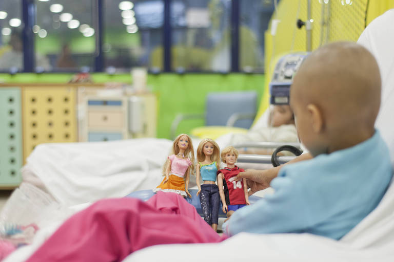Criança em tratamento para câncer interage com bonecos em cama de hospital