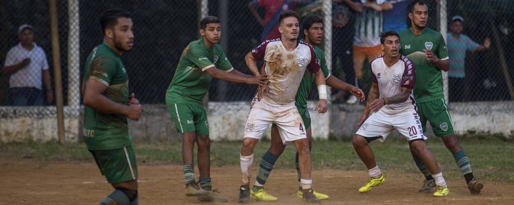 Jogadores disputam bola durante partida em campo de várzea, em São Paulo