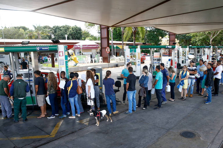 fila de pessoas pra encherem galões de gasolina em posto