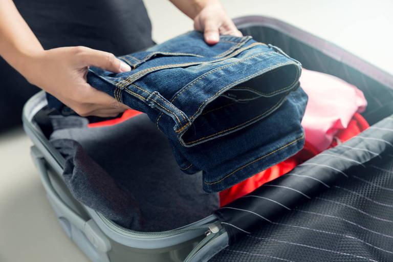 Pessoa colocando jeans dobrado em mala 