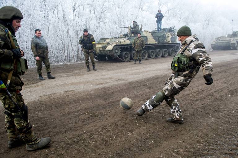 Homem com roupa de exército chuta bola em estrada de terra 