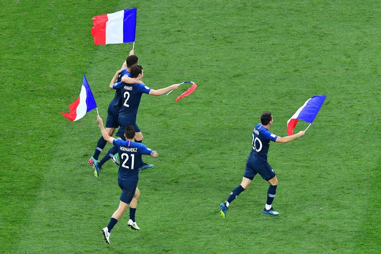 Quatro homens vestidos de azul andam em gramado com bandeiras da França