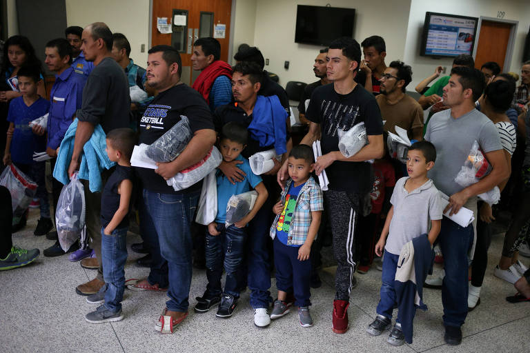 Cinco homens formam filas segurando envelopes em seus braços e acompanhando cinco crianças menores