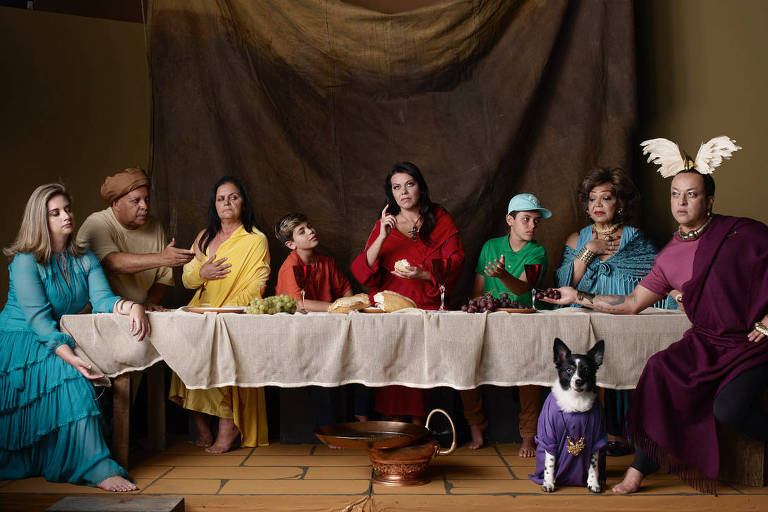 Personagens sentados em torno de longa mesa de jantar simulando cena similar à Santa Ceia