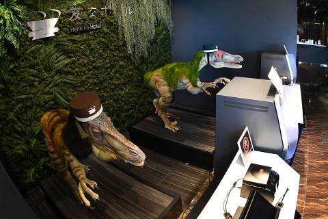 A pair of robot dinosaurs wearing bellboy hats welcome guests from the front desk at the Henn-na Hotel in Urayasu, suburban Tokyo on August 31, 2018. - The reception at the Henn-na Hotel east of Tokyo is eeriely quiet until customers near the robot dinosaurs manning front desk. Their sensors detect motion and they bellow: 