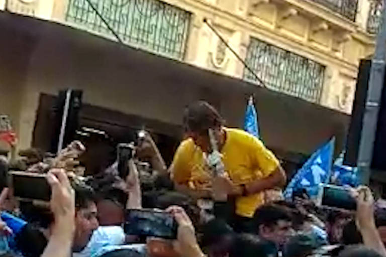 Bolsonaro, homem branco, de camiseta amarela em rua cheia de pedestres. Ele leva as mãos à barriga