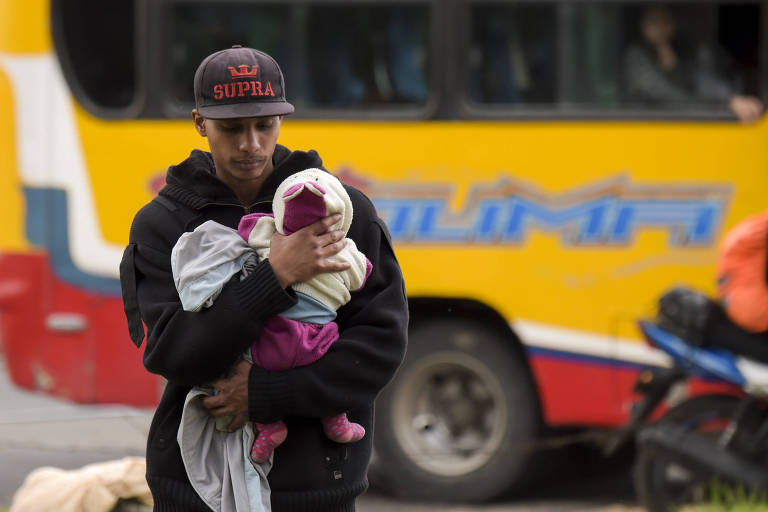 Homem de boné carrega um bebê distanciando-se de um ônibus amarelo