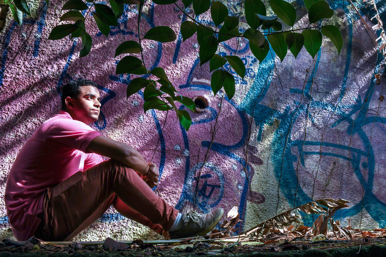 Steve Camilo Gomes de Azevedo, 26, sentado no chão sob as folhas de uma árvore