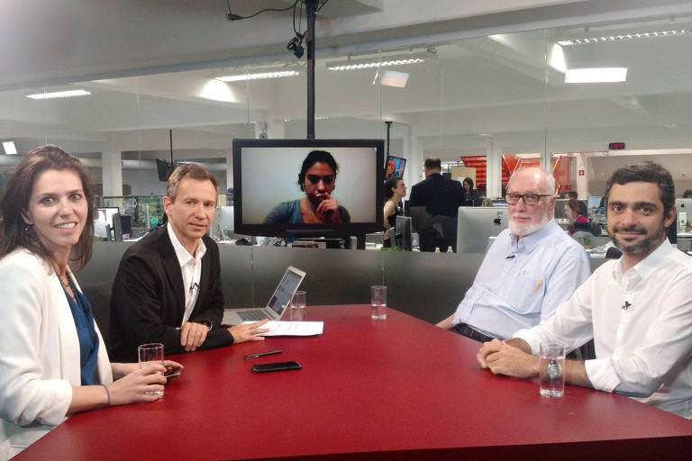 Sentados na mesa do estúdio da TV Folha, a repórter Thais Bilenky, o repórter especial Fernando Canzian e os colunistas Clóvis Rossi e Bruno Boghossian durante debate na TV Folha. Na tela da TV, a correspondente em Nova York, Danielle Brant.