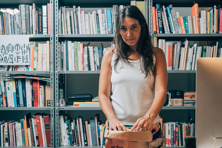 Mulher de camiseta branca em frente a prateleira de livros