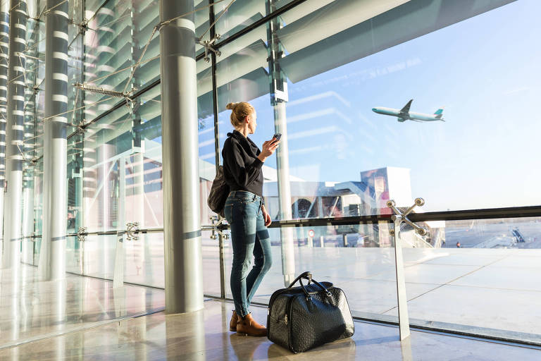 Mulher com celular na mão olha para avião em aeroporto