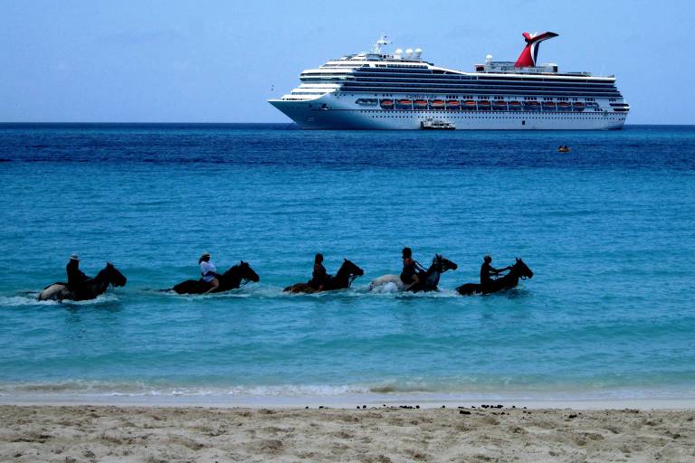 Pessoas andam a cavalo dentro da água em praia 