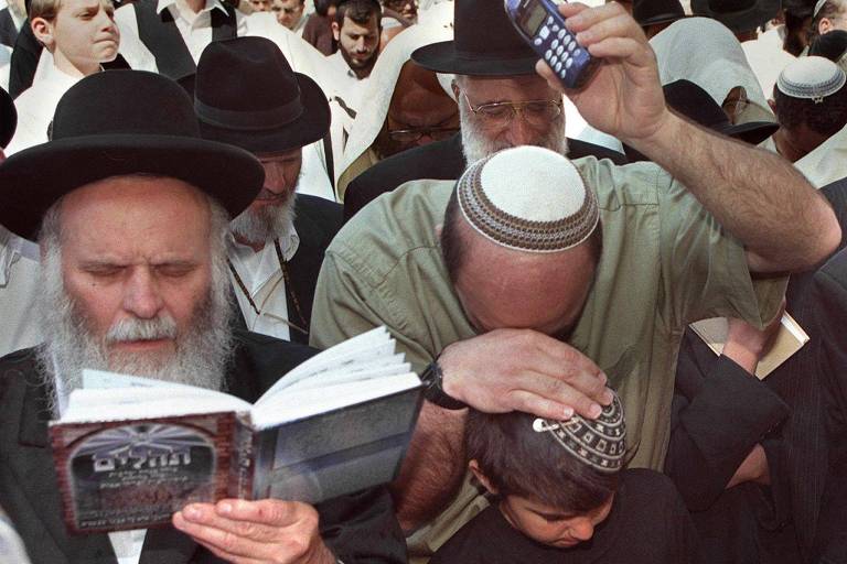 Homem segura celular perto de judeus ortodoxos que rezam na esplanada em frente ao Muro das Lamentações, em Jerusalém, durante a Páscoa judaica (Pessach) 