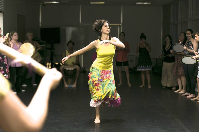 mulher de amarelo dança em meio a roda de instrumentos musicais