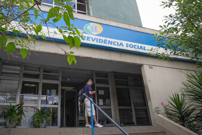 Fachada do INSS parcialmente coberta pelos galhos de uma árvore