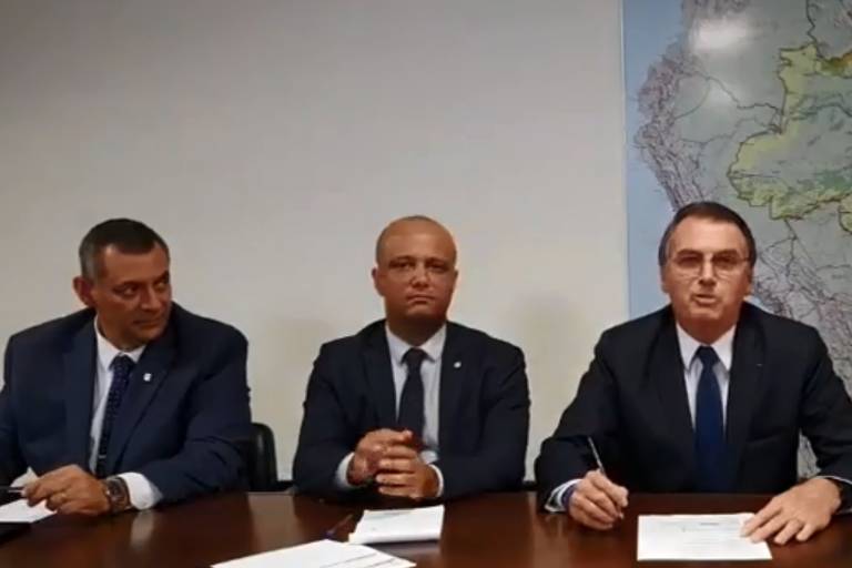 O presidente Jair Bolsonaro (PSL) em sua live semanal, ao lado do porta-voz, general Rêgo Barros, e do deputado Major Vitor Hugo (PSL-GO)