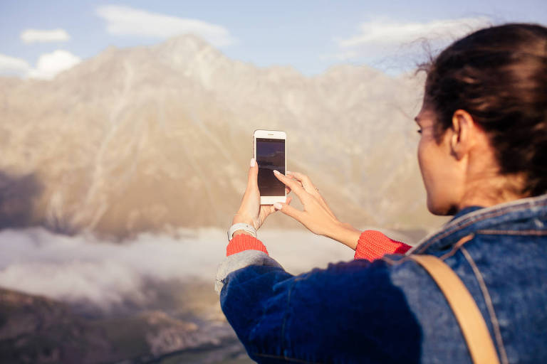 Young stylish girl makes photos and videos of traveling in the mountains for her blog and site on a sunny summer day. Concept of travel alone