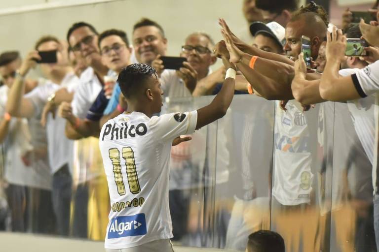 Após marcar o primeiro gol do Santos na Vila Belmiro, o atacante Rodrygo cumprimenta alguns torcedores santistas que se aglomeraram rente à grade de acrílico que separa a arquibancada do campo
