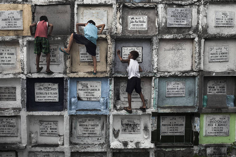 Meninos escalam lápides de um cemitério em Manila, capital das Filipinas; clique de Gustavo Gusmão integra 'Limbus', sua individual no MIS