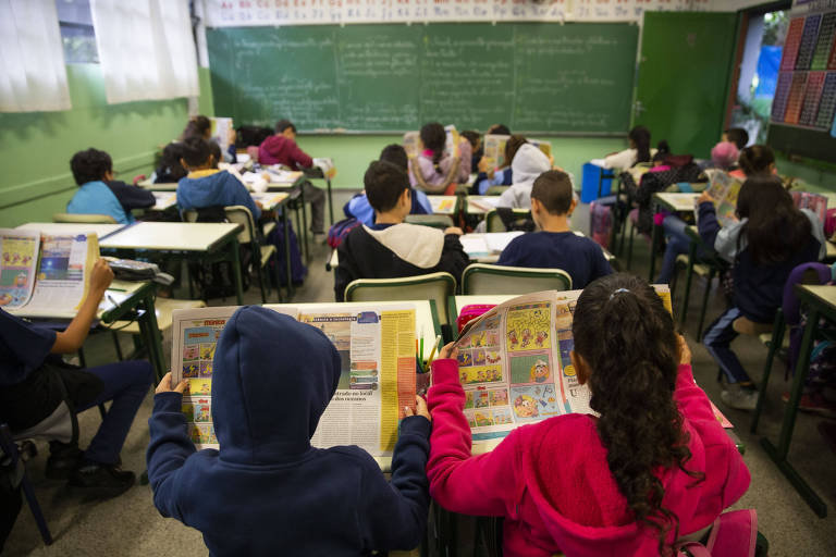 Crianças leem jornal em sala de aula
