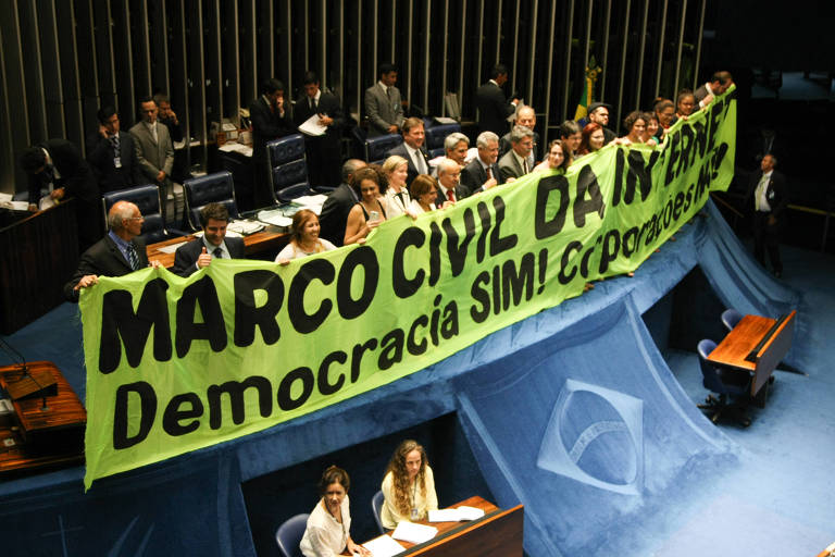 Grupo de cerca de 20 pessoas segura uma faixa amarela na parte da frente do plenário do Senado, onde se lê "Marco Civil da Internet. Democracia SIM".