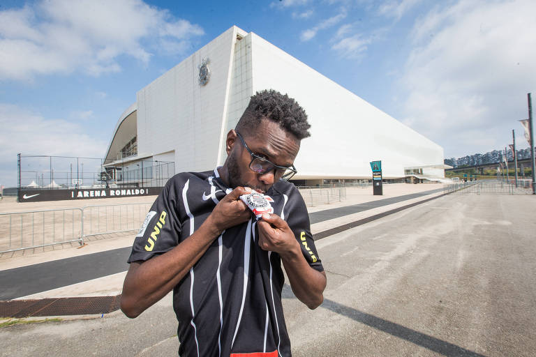 Lucas Conceição dos Santos beija a camisa do Corinthians em frente à arena de Itaquera, onde acompanha as partidas do time alvinegro na arquibancada ou à beira do gramado como gandula
