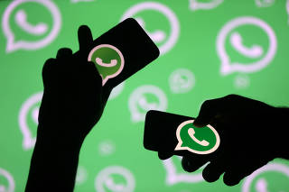 FILE PHOTO: Men pose with smartphones in front of displayed Whatsapp logo in this illustration