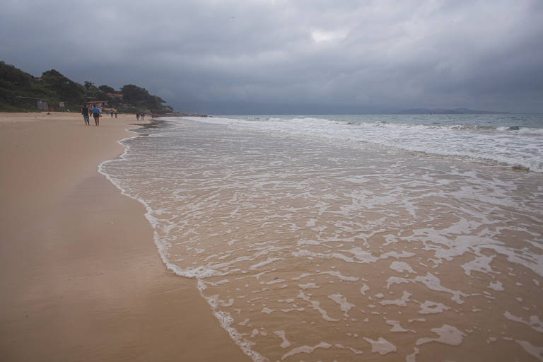 Água do mar quebrando na areia; ao fundo, banhistas caminham na praia