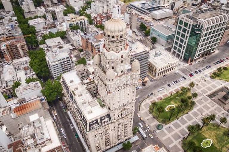 foto mostra vários prédios vistos de cima em grande centro urbano. à direita, praça com árvores