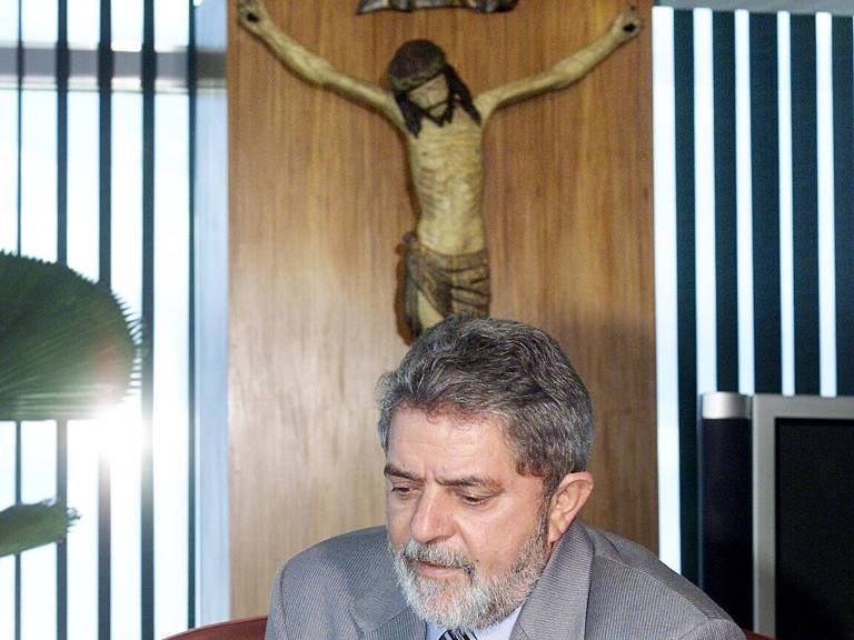 O então presidente Lula lê panfleto no Palácio do Planalto, em 2003, com crucifixo ao fundo