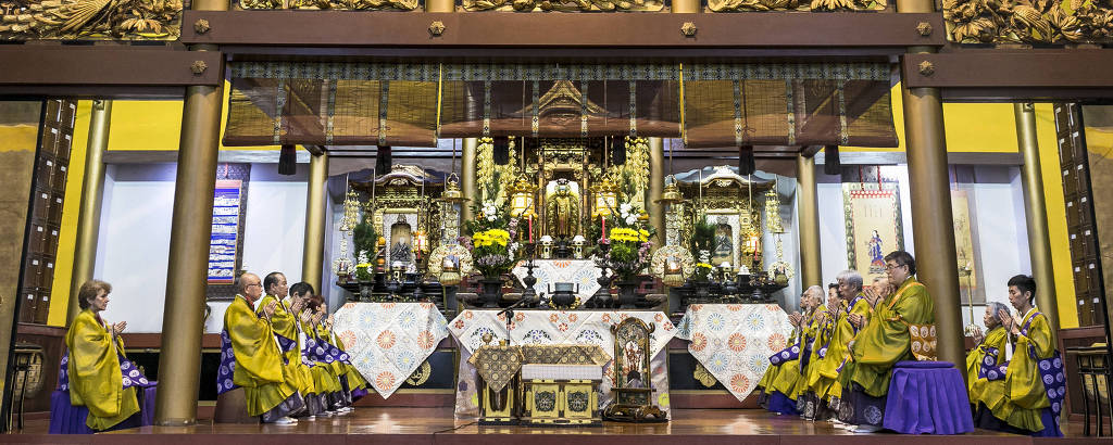 Monges de amarelo em altar de templo com muita madeira e dourado 