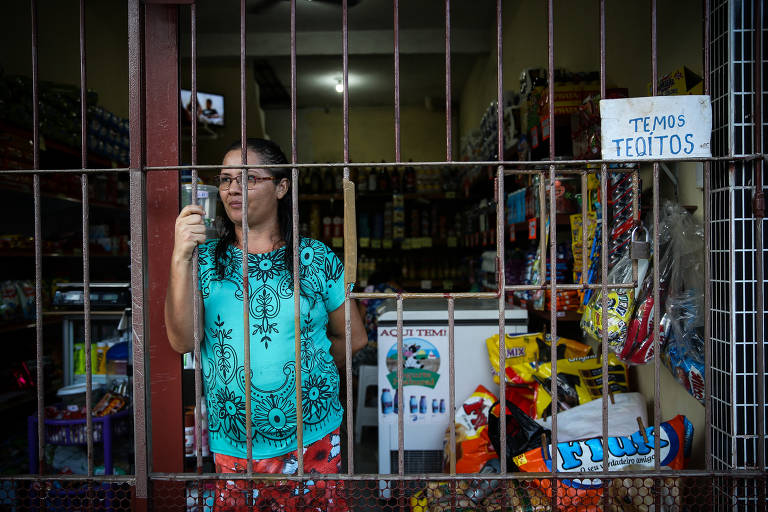 Caticilene Costa, 40, em sua mercearia em Ananindeua, coberta por grandes; os clientes recebem os produtos e pagam por uma portinhola