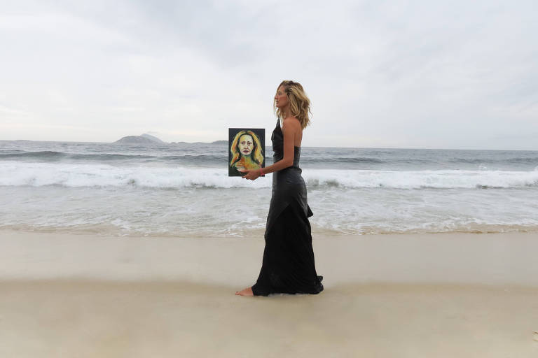 mulher em pé na praia segurando quadro