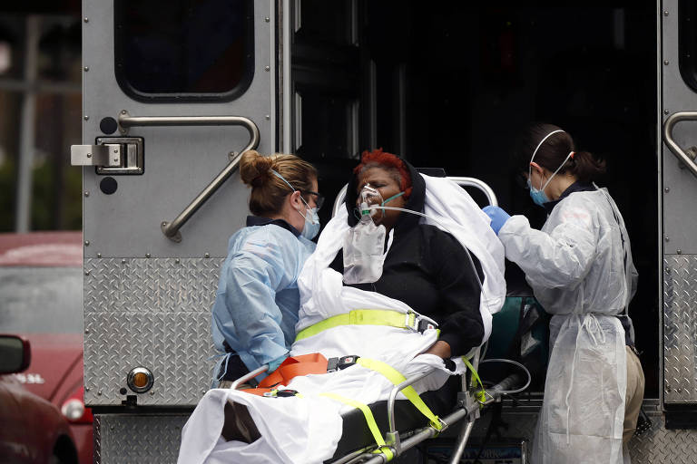 Com equipamentos de proteção, equipe médica coloca paceinte dentro de ambulância em Nova York, em meio à pandemia de coronavírus