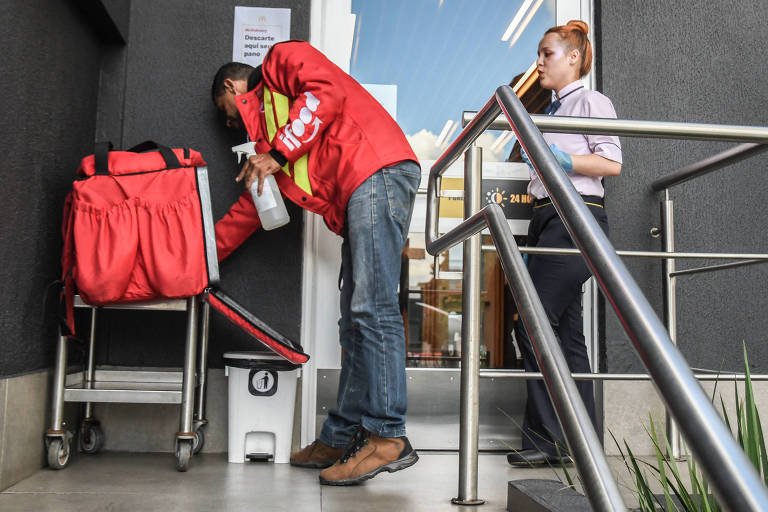 Vendas online se tornaram maioria após a pandemia; na foto, motoboy precisa limpar sua mochila de entrega antes de entrar na loja para buscar o produto 