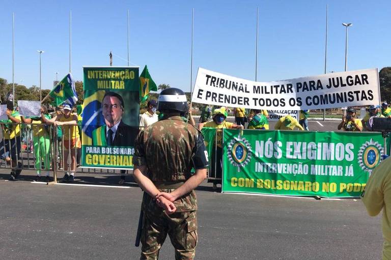 Apoiadores do presidente Jair Bolsonaro seguram cartazes a favor da intervenção militar e com foto do presidente