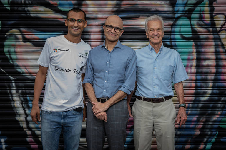 três homens sorriem para foto em frente a painel grafitado